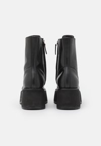 Botas de tobillo de cuero negro con una suela de plataforma gruesa, con cremalleras laterales y detalles de costura a lo largo de la parte posterior y los lados.