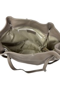 Jasnobrązowa skórzana torba typu tote z otwartą górą i wewnętrzną kieszenią na zamek. Charakteryzuje się miękką teksturą, kontrastowymi przeszyciami oraz solidnymi paskami.