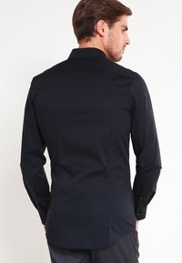 Zwart herenshirt met lange mouwen, standaardkraag, effen textuur, slim-fit ontwerp en knopenmanchetten. Geen zichtbare patronen of accenten.