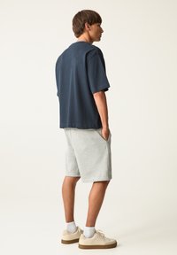 T-shirt oversize blu navy, maniche corte, tessuto in cotone. Abbinato a pantaloni corti grigio chiaro, tasche, texture morbida, e sneakers crema con suole marroni.