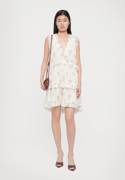 Blomstertrykt kjole i lyse kremfarget stoff, med volanger i kanten, dyp V-hals og lagdelt design. Kombinert med en brun håndveske.