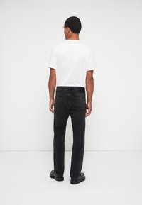 Vaqueros negros con un corte clásico y piernas rectas, combinados con una camiseta blanca lisa. El material parece de mezclilla y cuenta con dos bolsillos traseros.