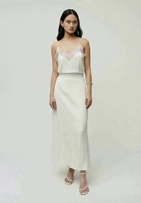 Elfenbeinfarbener Zweiteiler bestehend aus einem Spitzenbesatz-Cami und einem langen, figurbetonten Rock. Glattes Material mit Spaghettiträgern und minimalen Akzenten.