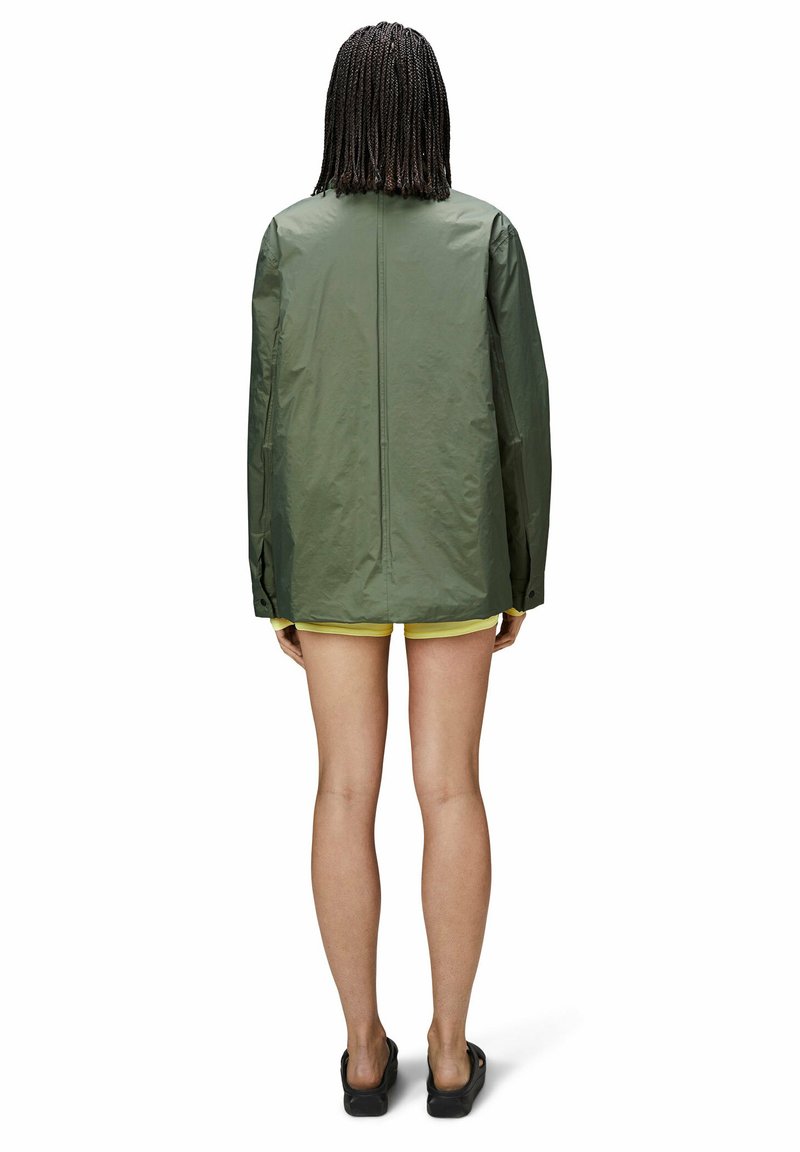 Veste imperméable verte avec une coupe ample, des manches longues et un ourlet droit. Texture lisse, détails minimalistes et une ventilation à l'arrière.