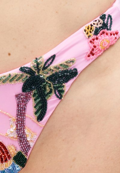 Tissu rose avec une broderie florale détaillée en perles et sequins porté sur l'épaule d'une personne.