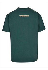 Mørkegrøn bomulds T-shirt med afslappet pasform, der har rund hals og korte ærmer. "UPSC⚡LE" tekst i beige på ryggen.