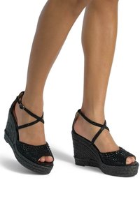 Sandali neri con tacco a cuneo, open toe, design intrecciato testurizzato e cinturini incrociati decorati con accenti lucidi.