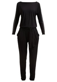 Combinaison noire à manches longues avec des clous argentés sur les manches, une ceinture nouée à la taille, des poches latérales et des jambes fuselées.