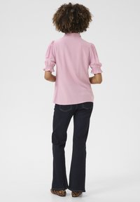 Svetloružová blúzka s krátkymi nafúknutými rukávmi a golierom, v kombinácii s tmavými rozšírenými džínsami a topánkami s leopardím vzorom. Hladký materiál, ležérny štýl.