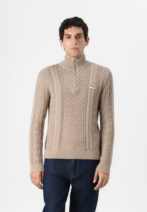Beżowy sweter dzianinowy z wysokim kołnierzem i zamkiem, ozdobiony teksturowymi wzorami takimi jak warkocze i romby, z prążkowanymi mankietami oraz detalem z logo.