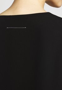 En persons övre rygg och nacke synliga, klädd i en svart topp med en horisontell vit söm nära skulderbladet.