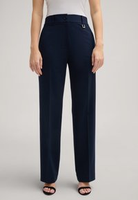 Marineblaue Hose aus glattem Stoff, mit taillierter Passform, einem einzelnen Knopfverschluss und einem dezenten metallischen Akzent am Bund.