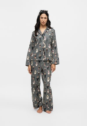Woman standing barefoot wearing black striped pajamas with printed small animal figures and a matching headband against a plain white background.