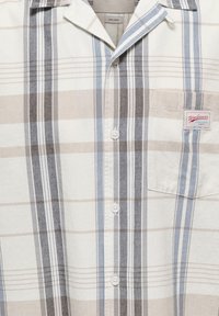Chemise à boutons avec des rayures verticales beige, bleues et gris foncé, dotée d’un col et d’une poche poitrine avec une étiquette "Workwear".