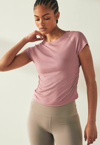 Top scurt roz deschis cu mâneci scurte, cu un design ajustat și detalii strânse pe lateral, asortat cu colanți bej cu talie înaltă, amândouă din material elastic.