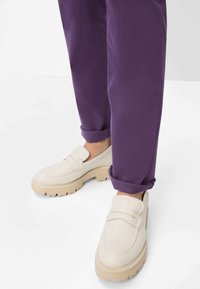 Mocassini in pelle bianca con suola spessa beige, caratterizzati da una semplice fascia sulla parte superiore, abbinati a pantaloni viola risvoltati.