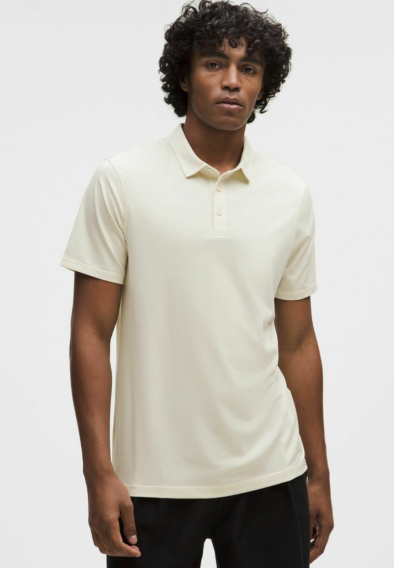 Beige poloshirt met een klassieke kraag, drieknopenlijst en korte mouwen. Soepele textuur en aansluitend ontwerp.
