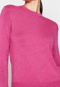 Upravený růžový svetr s kulatým výstřihem, žebrovanými manžetami a lemem. Pletená textura s hladkým povrchem, ukazující jednotnou barvu bez vzorů.