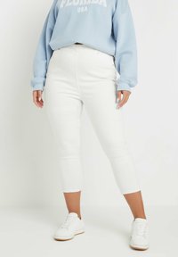 Jeans blancos hasta los tobillos con un diseño ajustado, combinados con un sudadera de gran tamaño en azul claro. Zapatillas blancas completan el look.