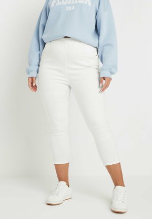 Jeans bianchi alla caviglia con un design aderente, abbinati a un felpa oversize azzurro chiaro. Sneakers bianche completano il look.