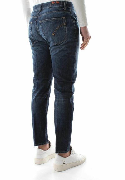 Jeans in denim blu con una vestibilità slim, dotati di tasche posteriori e dettagli di cucitura sottili. Abbinati a sneaker bianche su uno sfondo chiaro.