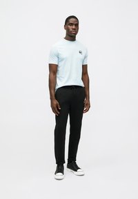 Gaiši zila īsās piedurknes T-kreklu ar mazu grafisku logo uz krūtīm, saskaņots ar melnām sporta biksēm ar auklu un melniem treneriem.