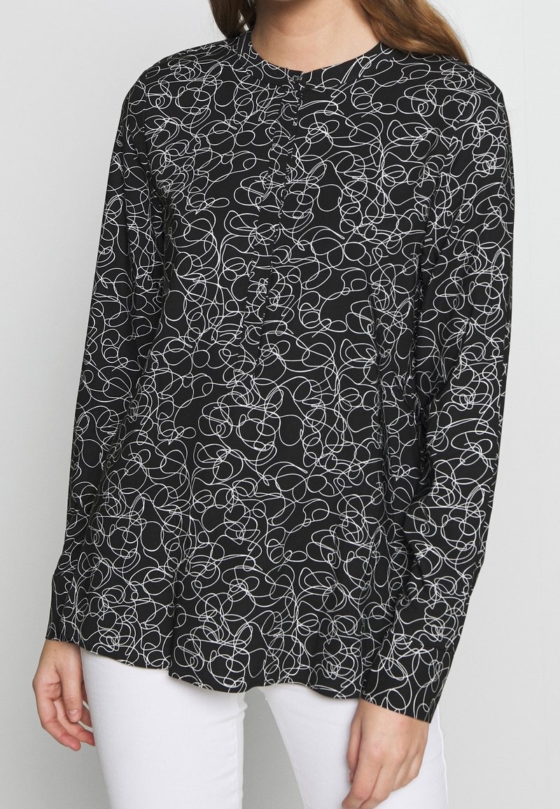 Chemise noire à manches longues avec un motif de lignes abstraites blanches, col rond et fermeture par boutons. Tissu doux, coupe décontractée.