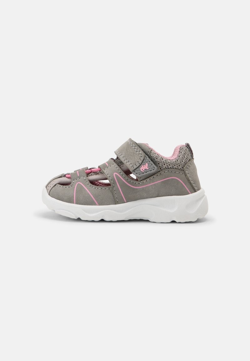 Zapatilla atlética gris con acentos en rosa y una correa de velcro. Presenta una parte superior texturizada y una suela blanca acolchada para brindar comodidad y soporte.
