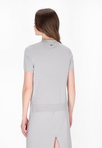 Grå kortærmet sweater med en glat, skinnende overflade. Har et tætsiddende design og ribbede kanter. Bagsiden af halsudskæringen har et lille logomærke.
