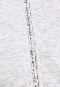 Sweat-shirt zippé gris clair avec un tissu texturé, doté d'une fermeture éclair métallique argentée sur le devant et de deux poches latérales.