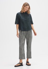 Camicia a maniche corte, button-up, verde scuro abbinata a pantaloni ampi a righe bianche e nere e sandali neri. Dettagli del tessuto testurizzato visibili.