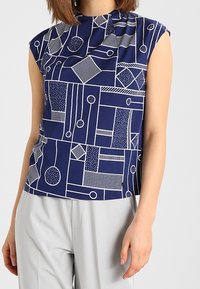 Navy blue sleeveless top featuring a geometric white pattern with circles, lines, and shapes. Smooth fabric with a round neckline.