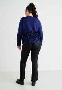 Blauwe pullover met een gradient luipaardprint, zachte textuur en geribde manchetten, gecombineerd met zwarte slimfit broek en stevige zwarte schoenen.