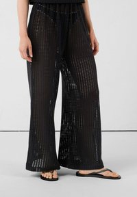 Pantalones de punto negros, ligeros, de tejido suelto, con piernas anchas y una cinturilla elástica, con un diseño transparente y corte recto.