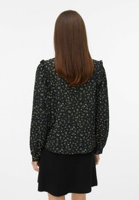 Blusa nera a fiori con maniche lunghe, caratterizzata da piccoli fiori verdi e bianchi, spalle arricciate e una silhouette fluida. Gonna nera sottostante.