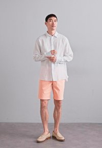 Leichtes, durchscheinendes weißes Hemd, pfirsichfarbene Shorts und beige Slipper. Glattes Material, lockere Passform und lässiger Stil.