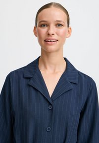 Námornícky pruhovaný košeľa s výstrihom do V a dvomi gombíkmi, vyrobená z hladkej tkaniny, s uvoľneným strihom a minimalistickým dizajnom.