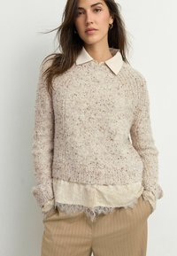 Švarkelis iš šviesiai beige spalvos megztinio su tekstūruota paviršiumi, raukšlėtais rankogaliais ir baltu apykakle po juo. papildytas šviesiai beige dryžuotais keliais.