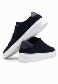 Marineblaue Wildleder-Sneaker mit weißer Gummisohle, ausgestattet mit einer glatten grauen Fersenakzent und passendem Schnürsenkel. Runder Zehenbereich.