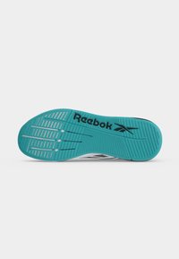 Τυρκουάζ σόλα παπουτσιού Reebok με μαύρο λογότυπο και γραμμικά αυλακωτά σχέδια για πρόσφυση και ευκαμψία σε λευκό φόντο.