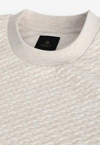Lys beige struktureret skjorte med et hævet diamantmønster, ribbet krave og et sort mærke med brandnavnet "NEXT."
