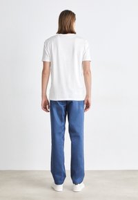 Camiseta blanca de algodón con mangas cortas, combinada con pantalones azul claro, de corte recto y con bolsillos frontales. Lleva puesta unas zapatillas blancas.