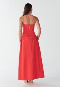 Punane maxi kleit rihmadeta disainiga, keha vormiv ülakeha ja tagant tõmblukuga. Sile tekstuur ja voolav siluett.