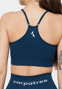 Jūras zilas sporta krūšturis ar gludu tekstūru, ar divām plānām siksnām un mazu baltu logotipu aizmugurē.