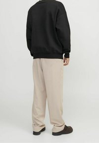 Černá mikina s kulatým výstřihem, volný střih a žebrované manžety, kombinovaná s béžovými širokými kalhotami a tmavými botami.