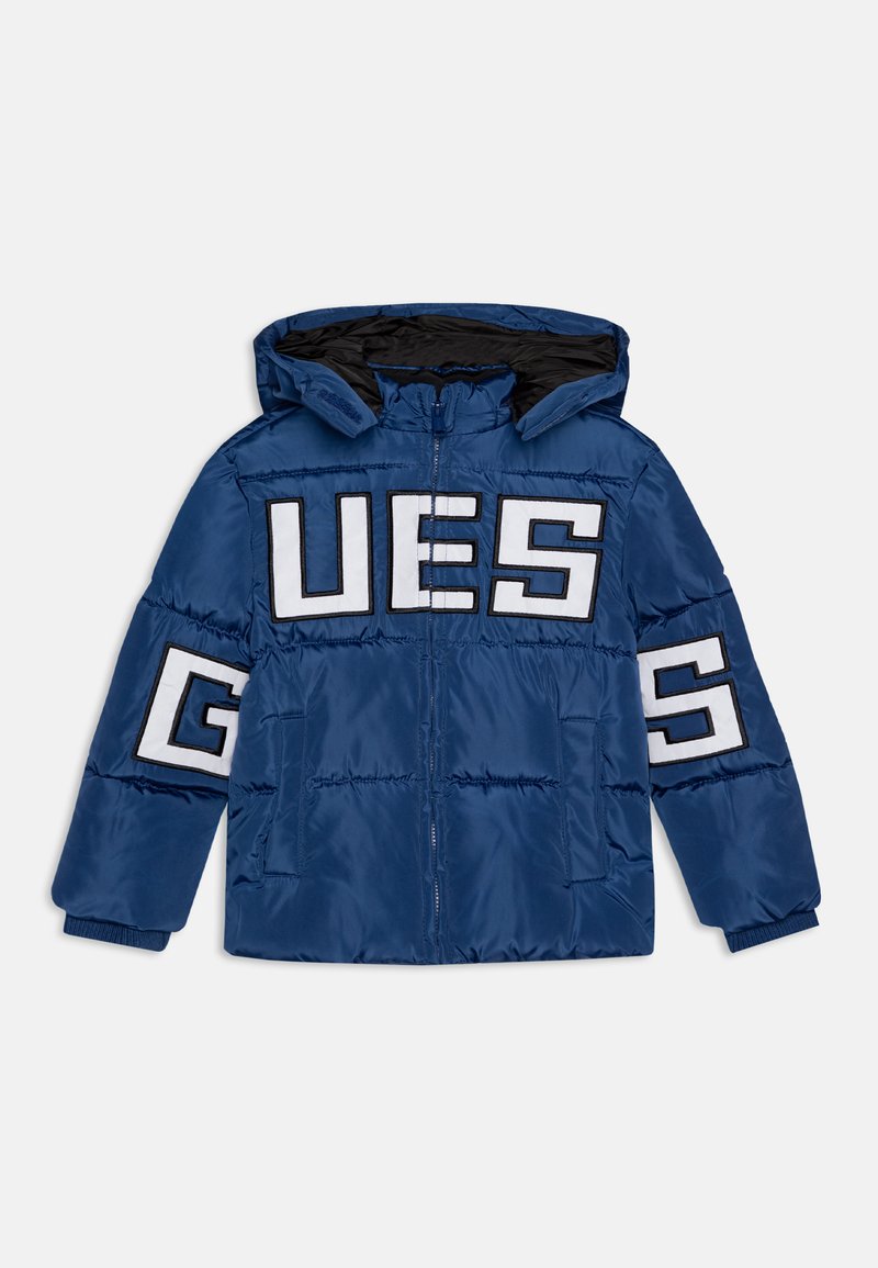 Giacca impermeabile blu con cappuccio, grande scritta bianca "GUESS", polsini elasticizzati e chiusura con zip. Finitura liscia con dettagli trapuntati.