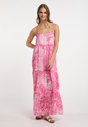 Abito lungo rosa con motivi floreali e paisley, tessuto leggero, spalline sottili e vestibilità ampia. Abbinato a sandali bianchi.