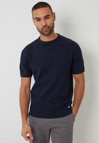 Suéter de punto de manga corta en color navy, con un patrón texturizado de diamantes, cuello redondo y una etiqueta de la marca sutil en el dobladillo.