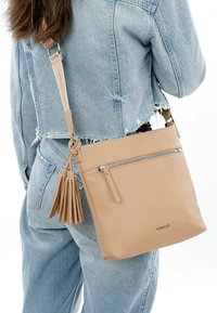 Beige leather crossbody bag with a zippered front pocket and tassel accent. Smooth texture, rectangular shape, detachable strap, and metallic hardware.