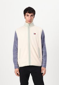 Lys beige fleecevest med høy krage og frontglidelås. Har to sidelommer, grå detaljer og en liten logo på brystet.